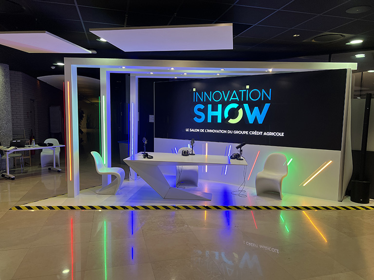 Photo de la Radio Live pour le salon Innovation Show du Crédit Agricole. Un espace triangulaire éclairé par des néons de différentes couleurs.